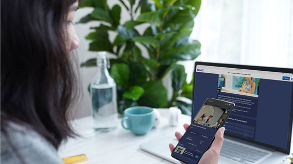 Female sitting in front of a laptop with a mobile device in her hand
