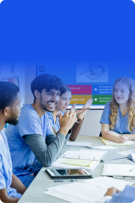 A blue-tinted photograph of healthcare students in scrubs sitting around a conference table engaged in a lively discussion, with a Kahoot! presentation visible on a screen in the background